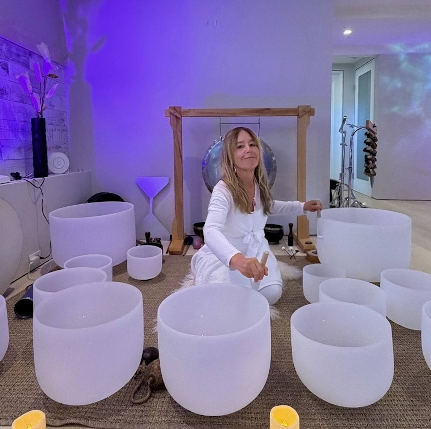 Gina Lola seated among crystal singing bowls in a sound healing studio