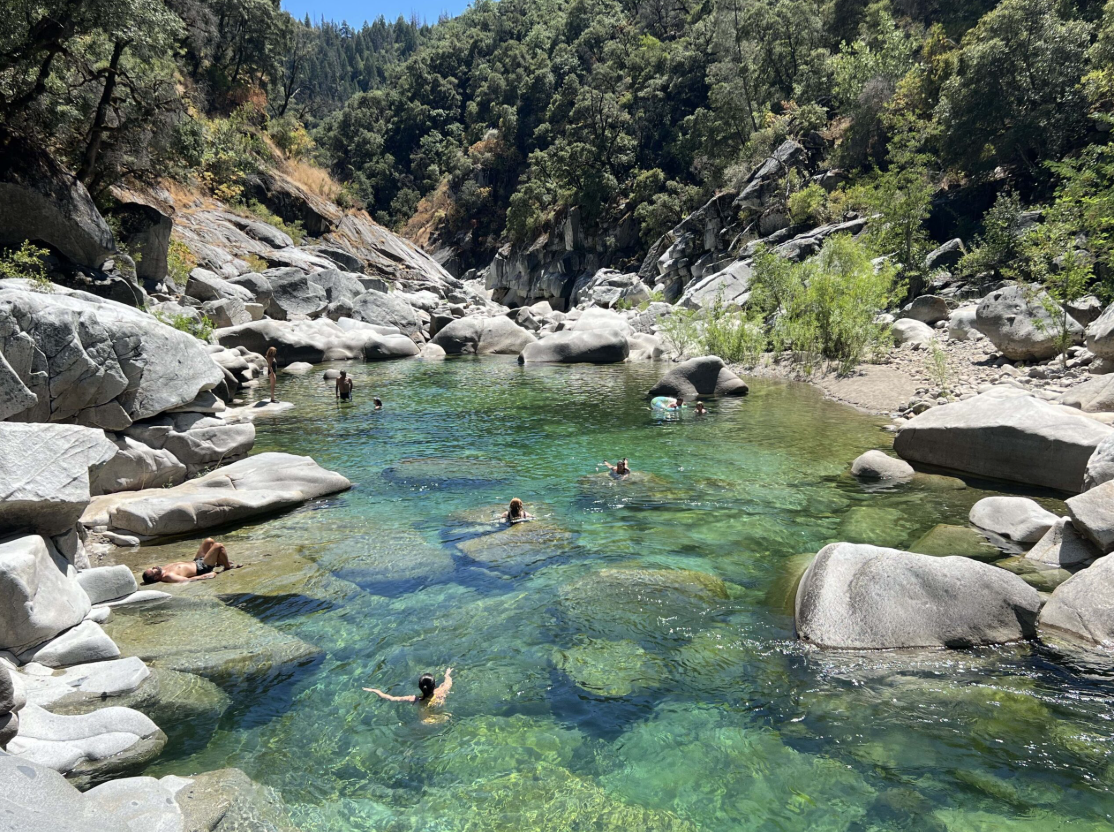 Swimmers in a clear emerald swimming hole on the Yuba River surrounded by granite boulders